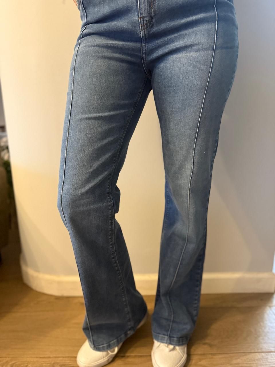Persona que viste jeans azules con detalle de costura y zapatillas blancas.