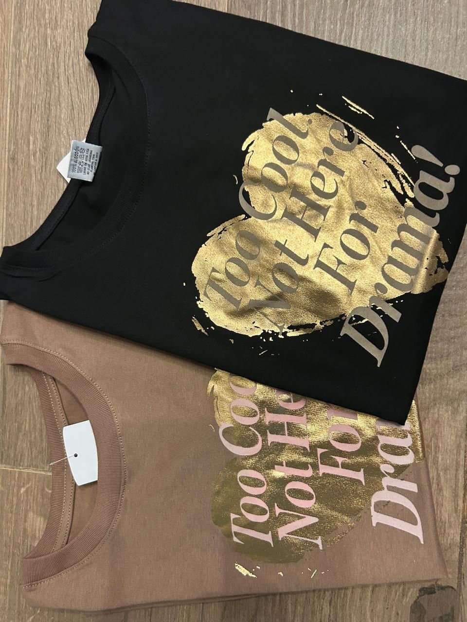 Dos camisetas, negra y tostada, con gráfico de corazón dorado y el texto