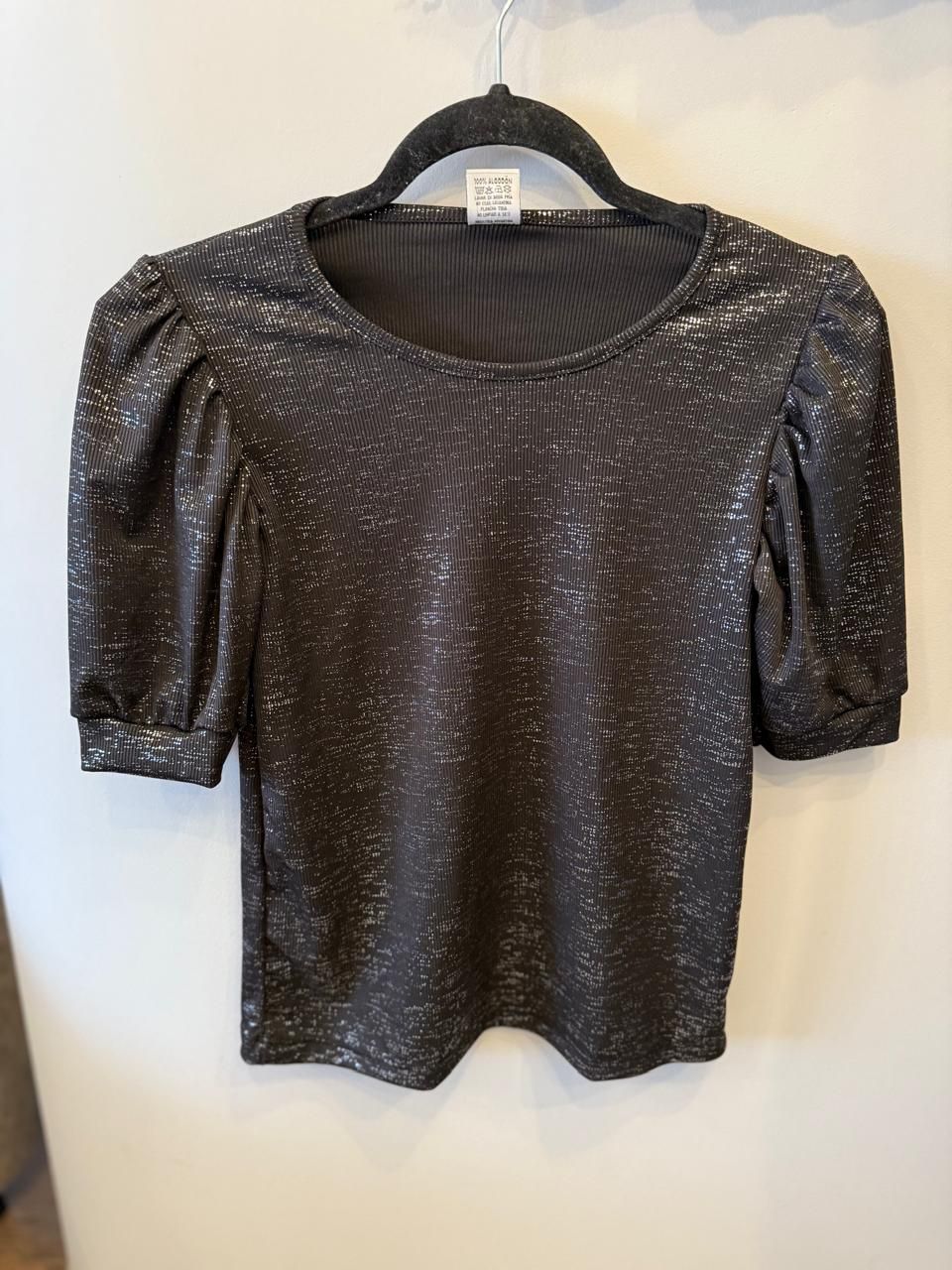 Top negro brillante con mangas cortas abullonadas en percha negra.