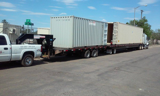 A white truck is towing a large shipping container