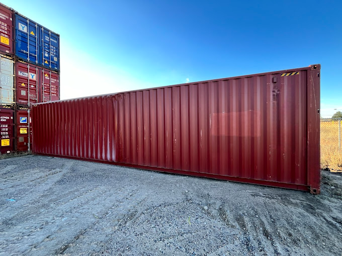 A large red shipping container is sitting in a gravel lot.