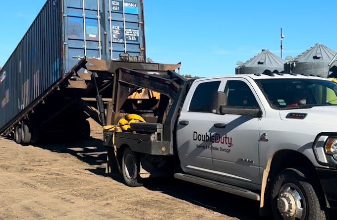 A double duty tow truck is carrying a container on a trailer.