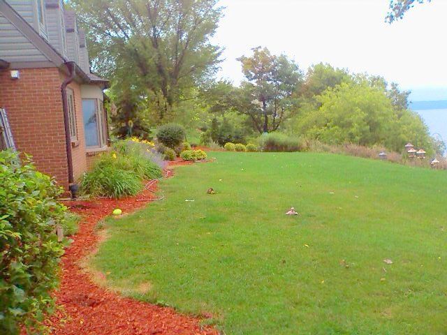 A large lawn with a house in the background and a lake in the background.