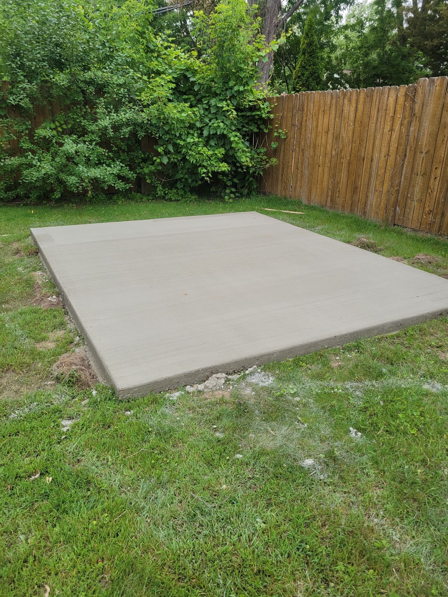 A concrete slab is sitting on top of a lush green lawn next to a wooden fence.