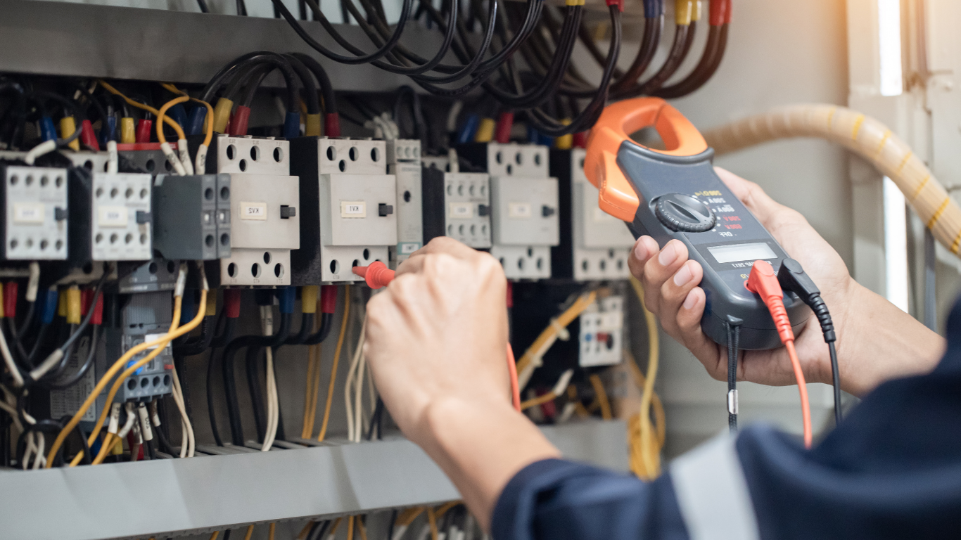 A brown and white tabby cat sits comfortably on a wooden floor near a doorway.
