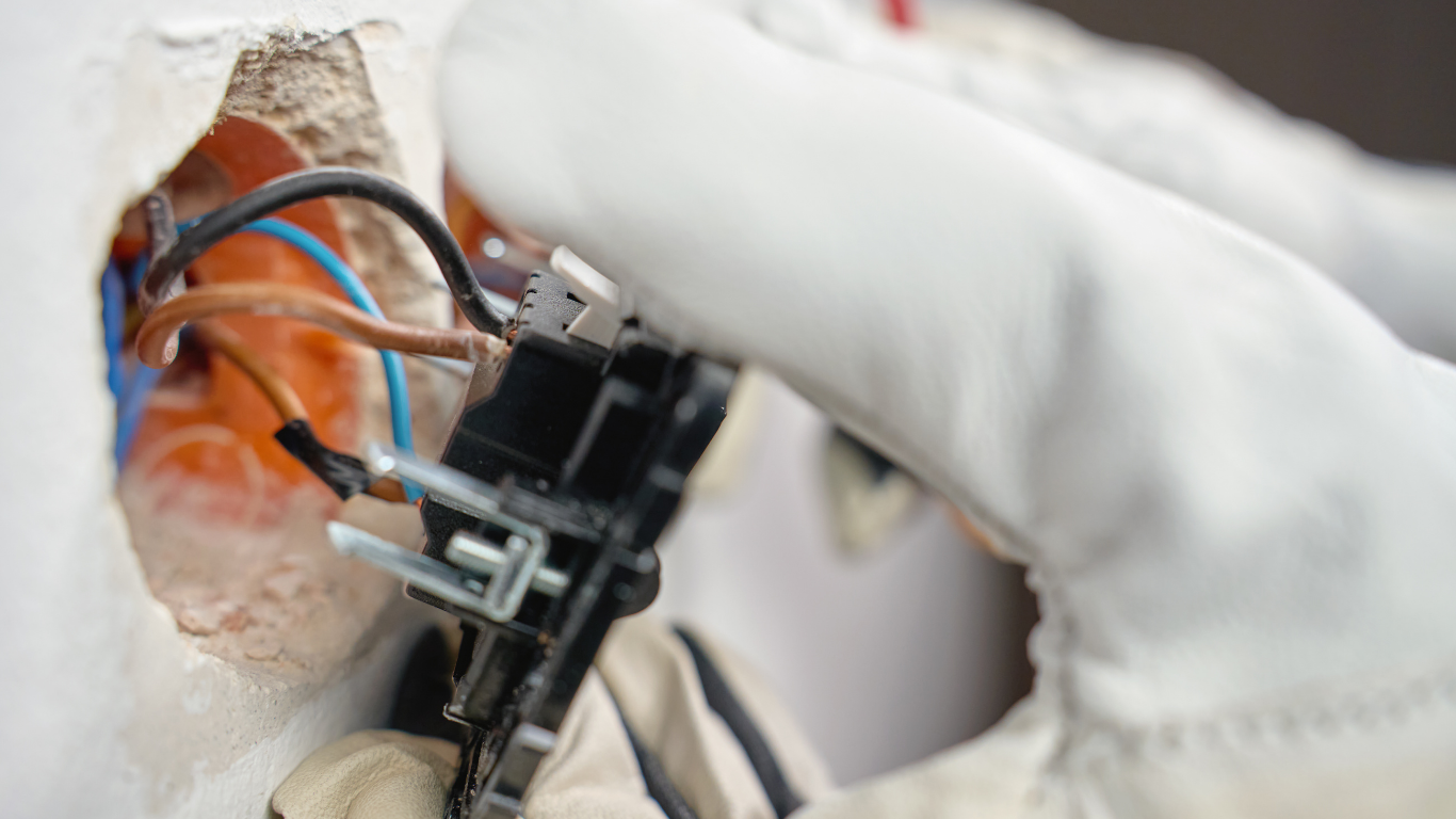 A brown and white tabby cat sits comfortably on a wooden floor near a doorway.