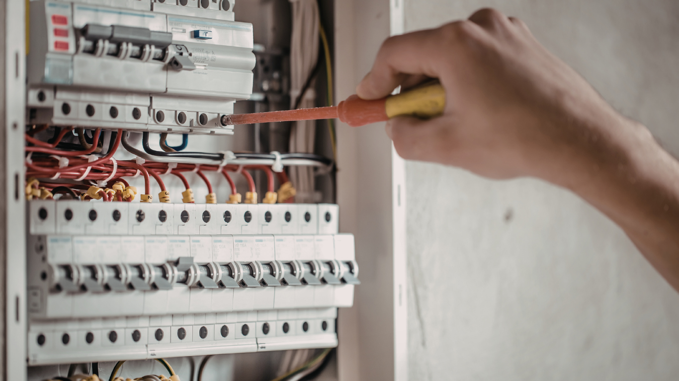 A brown and white tabby cat sits comfortably on a wooden floor near a doorway.