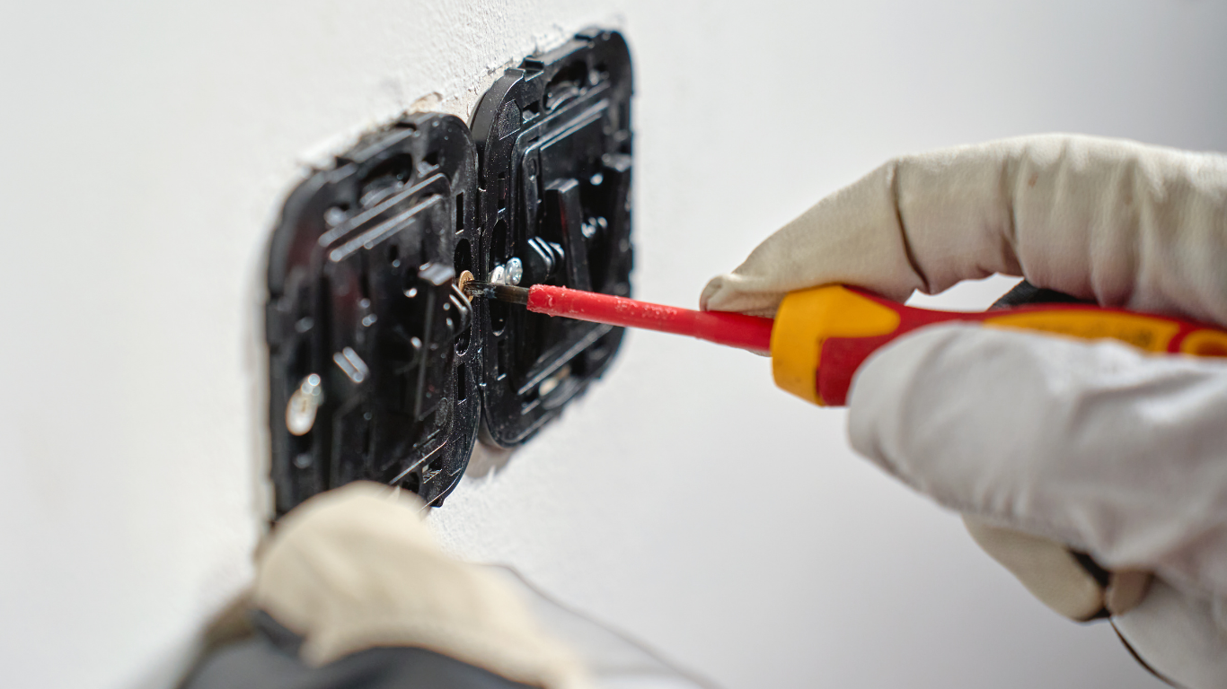 A brown and white tabby cat sits comfortably on a wooden floor near a doorway.