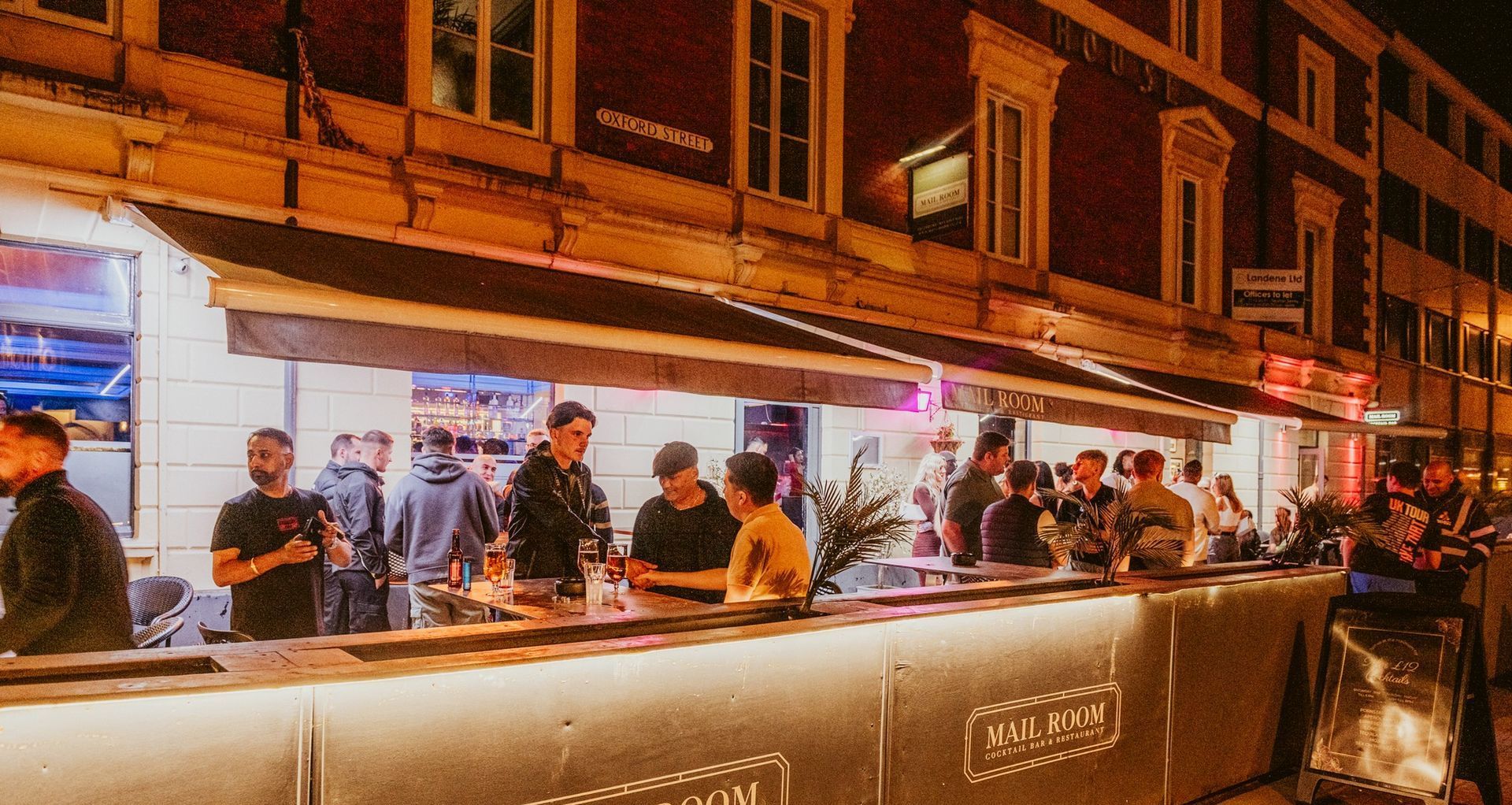 A group of people are sitting at a bar in front of a building.