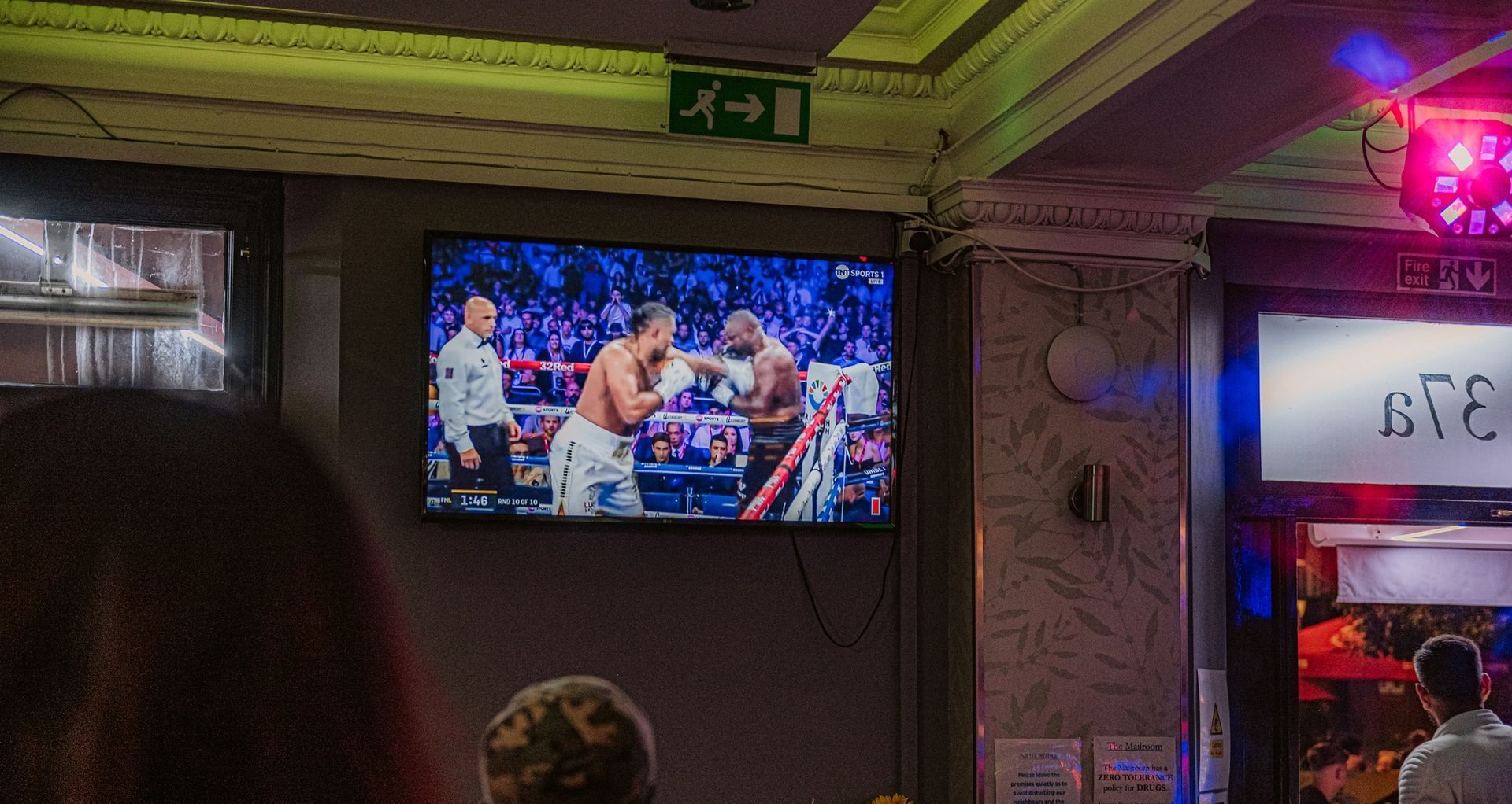 A group of people are watching a boxing match on a television.