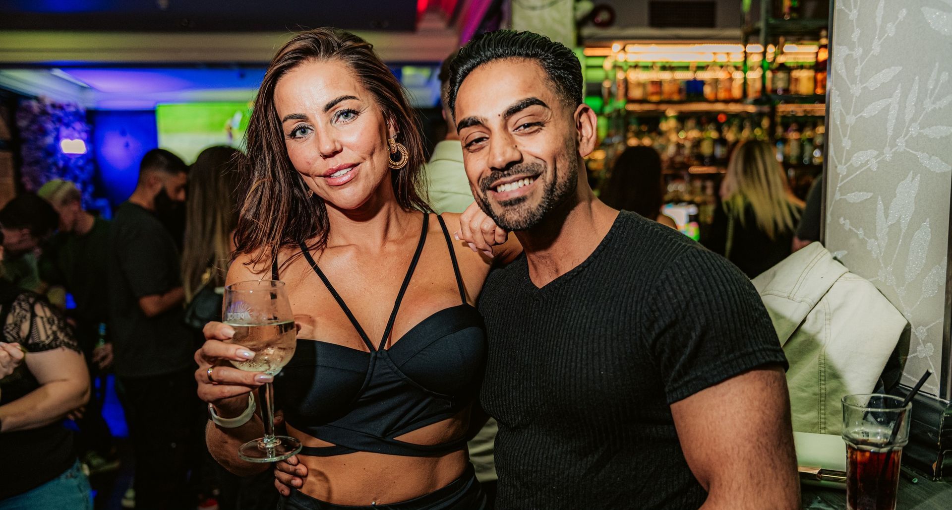 A man and a woman are posing for a picture at a party . the woman is holding a glass of wine.
