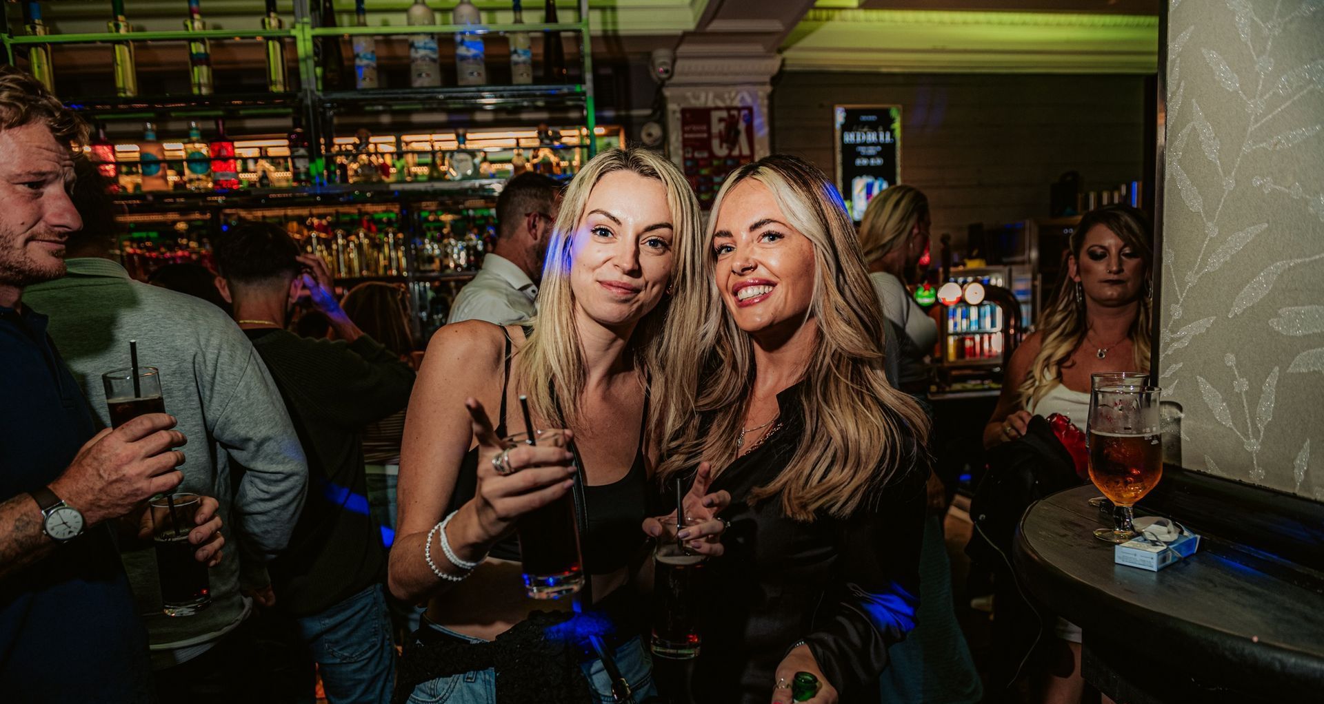 Two women are standing next to each other in a bar holding glasses of wine.