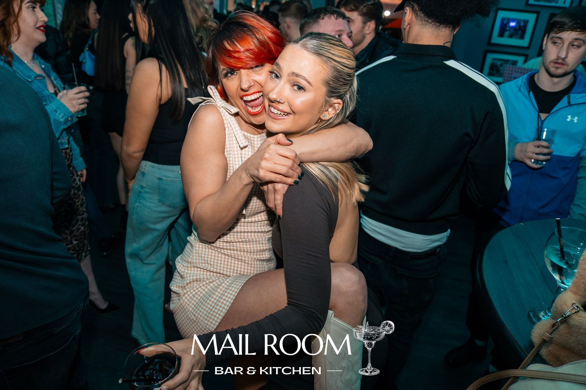 Two women are hugging each other in a crowded room at a party.