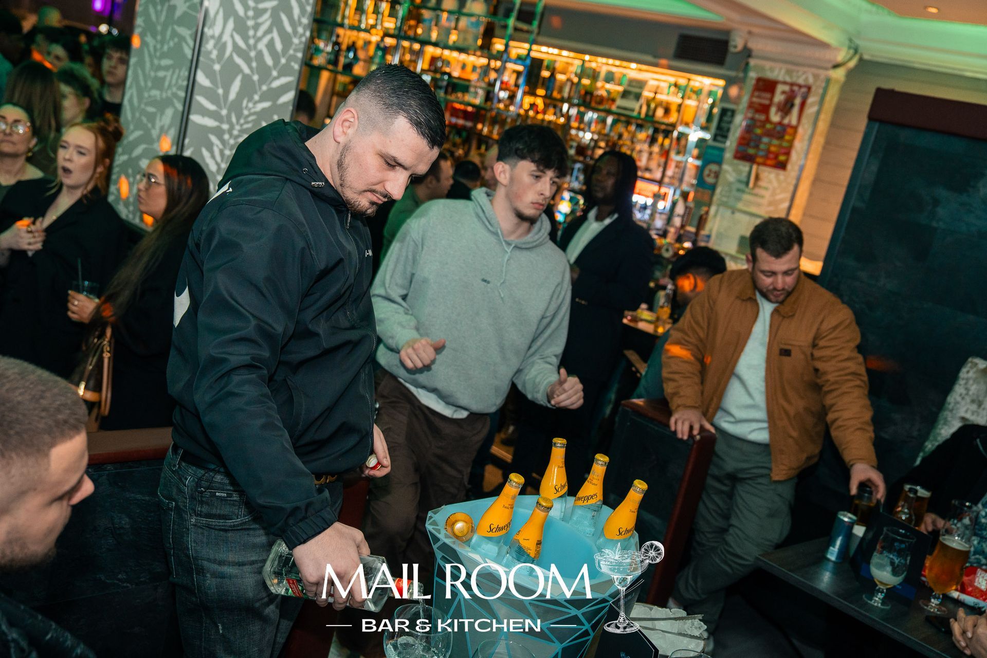 A group of men are standing around a bucket of beer in a bar.
