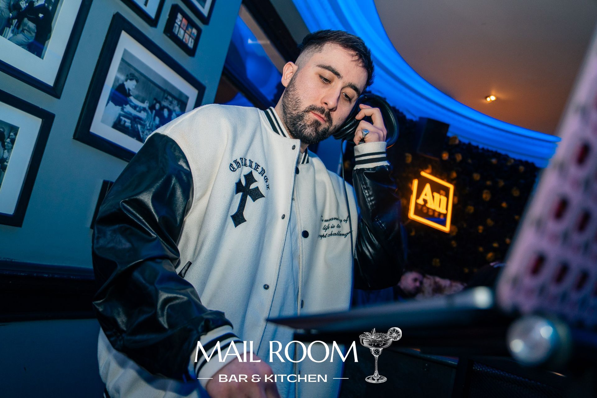 A man in a leather jacket is standing in front of a dj booth.
