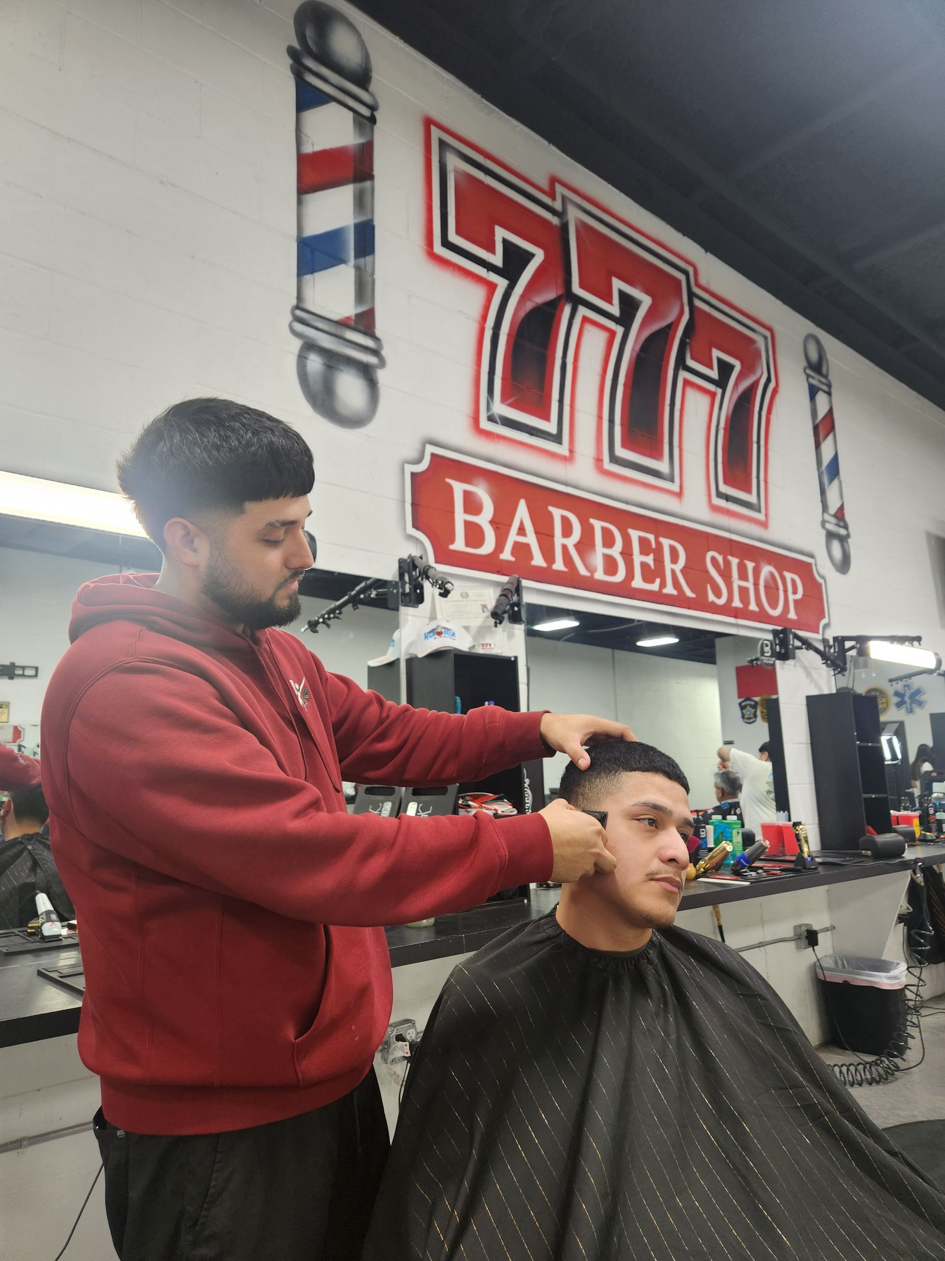 A barber giving a haircut at the 777 Barber Shop. The barber is using clippers.