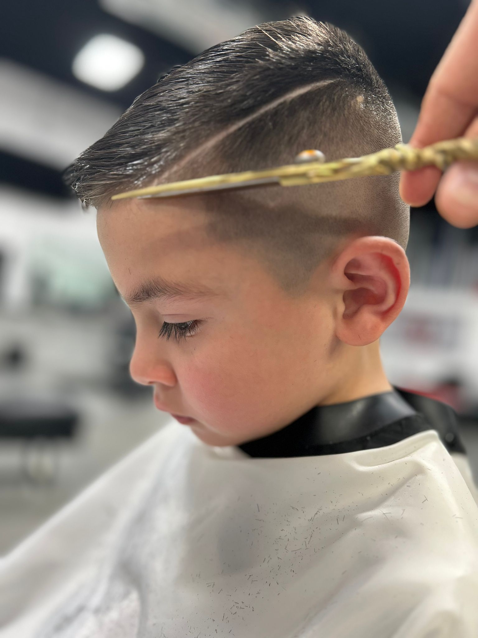 Boy getting a haircut; barber holding scissors, cutting hair. Salon setting.