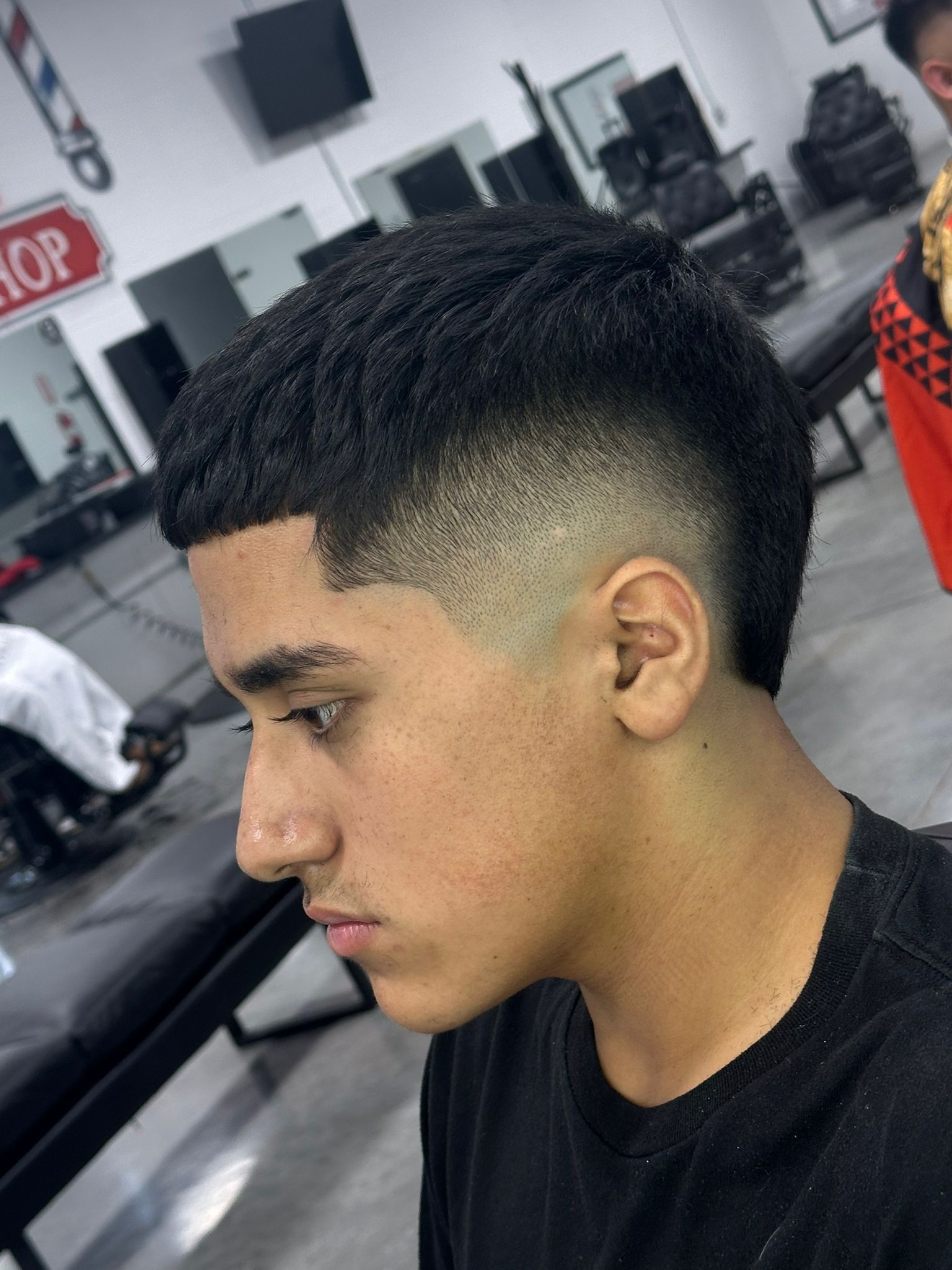 Young man with a faded haircut at a barbershop. He has dark hair, a fade on the sides, and is looking down.