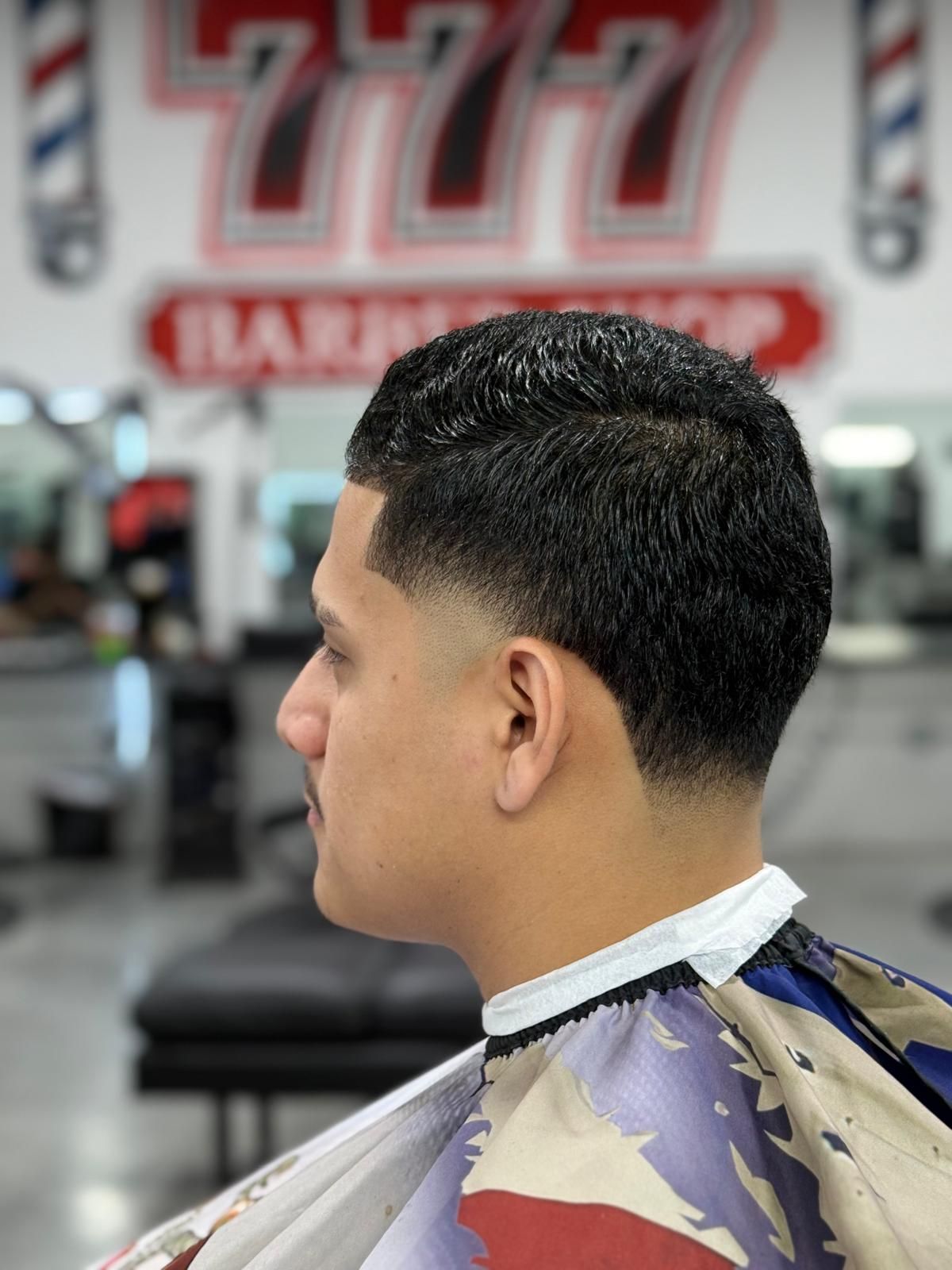 Man with a faded haircut at a barbershop, wearing a barber cape.