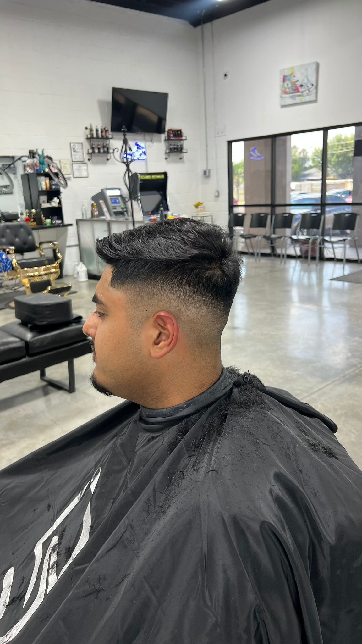 Man with a faded haircut in a barber shop, wearing a black cape.