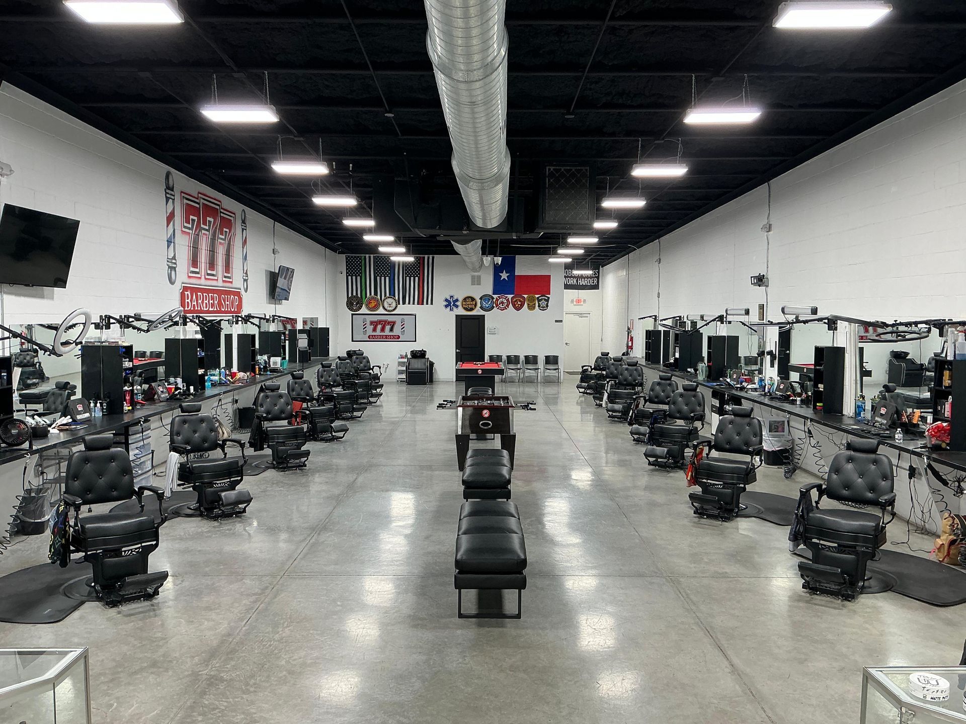 Interior of a barbershop with rows of barber chairs and mirrors. Black ceiling and white walls.