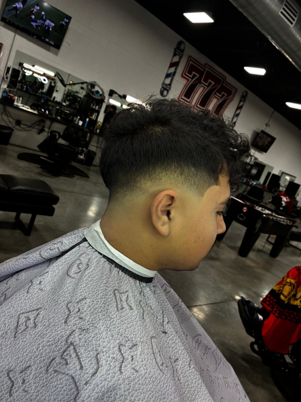 Boy with a faded haircut at a barbershop, wearing a cape.