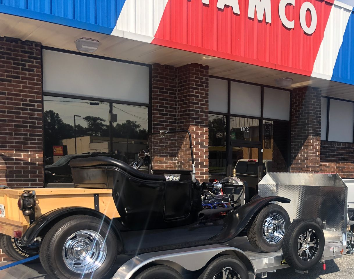 Classic black hot rod on a trailer outside an AAMCO storefront.