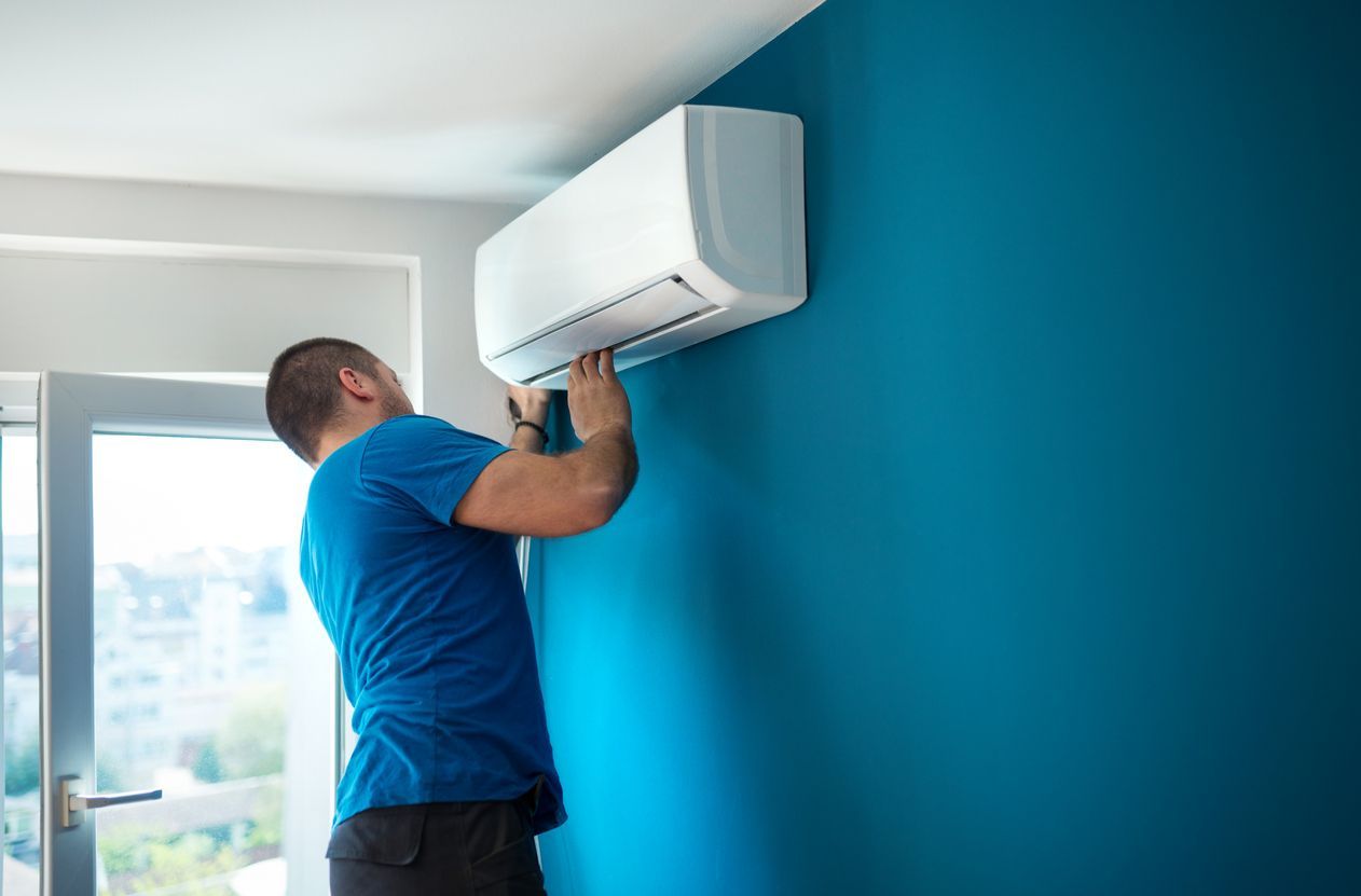 Technician installing a white wall-mounted air conditioner in a blue room