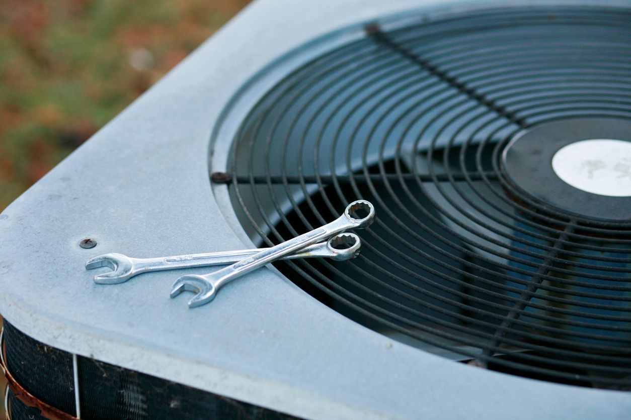 Two wrenches resting on a large outdoor air conditioner unit with a fan grille