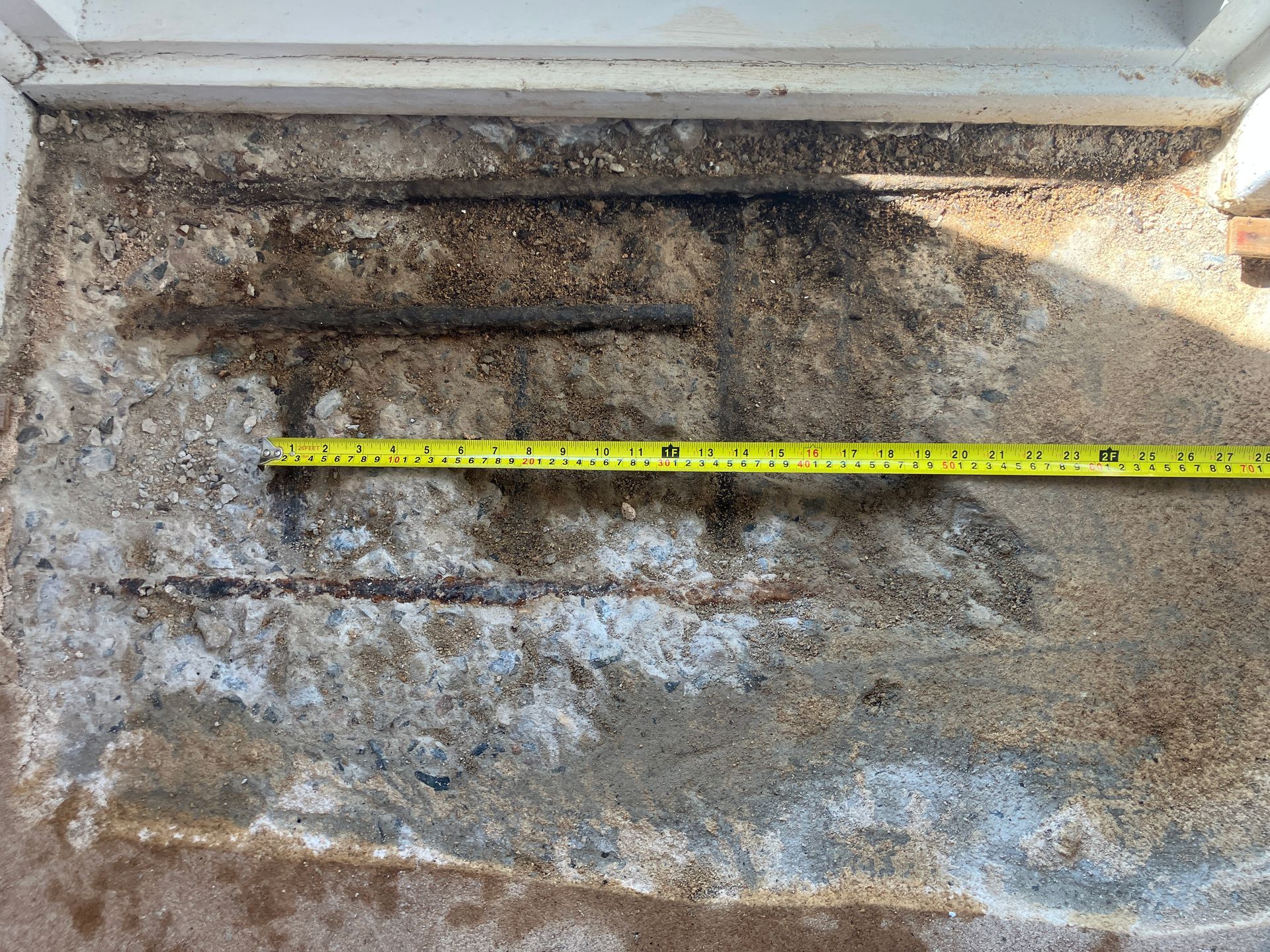 A concrete step with three recessed grooves, showing wear and white salt stains. A measuring tape is on the step.