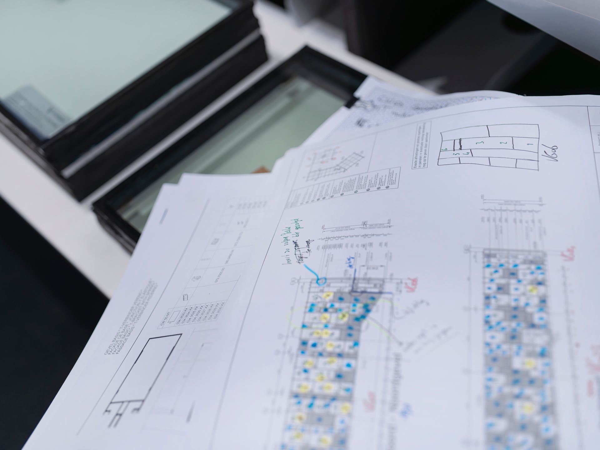 Architectural blueprints with a stack of windows in the background.