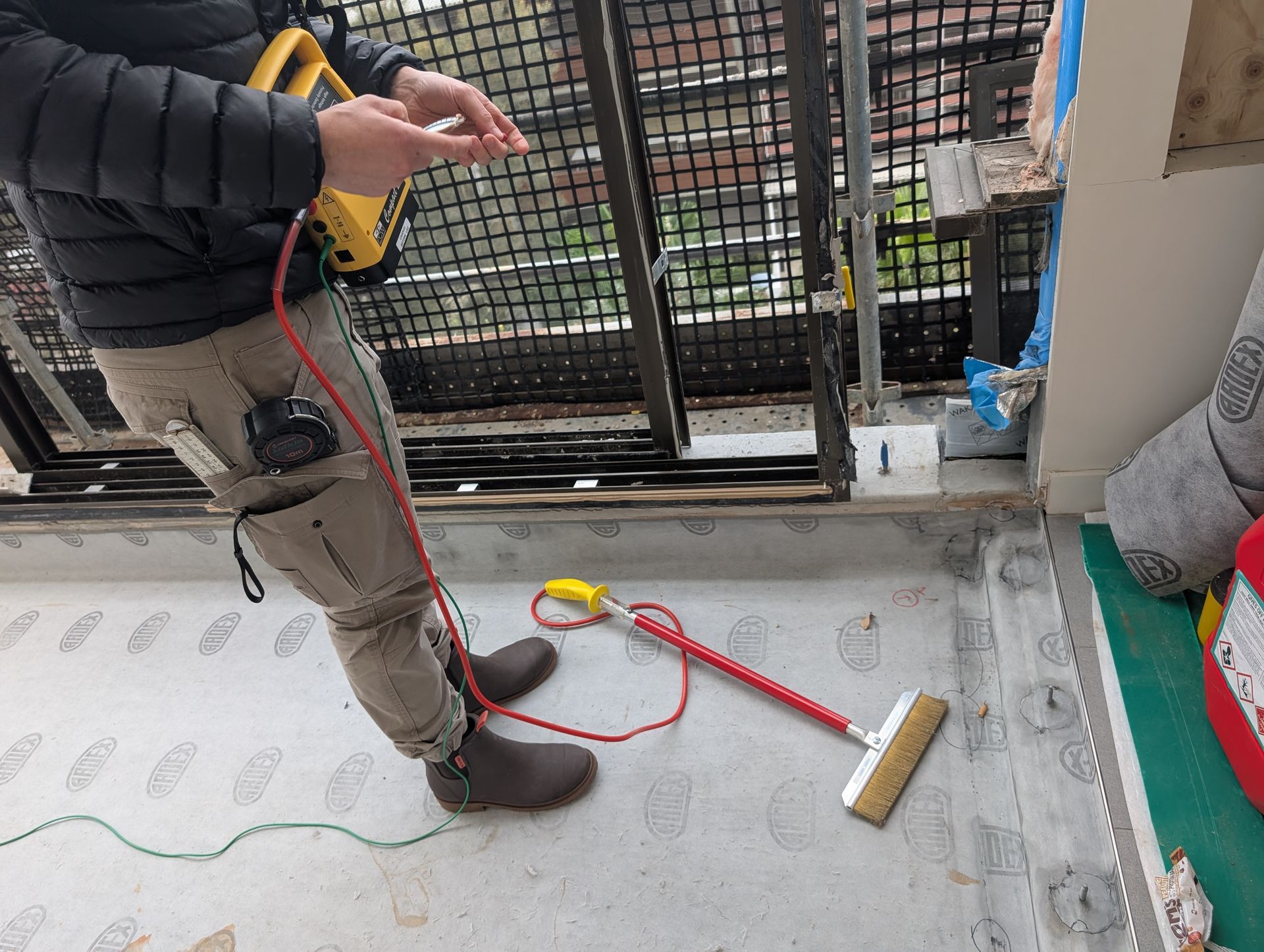Person using a floor testing tool on a balcony. A red cable and a yellow handheld device are visible.