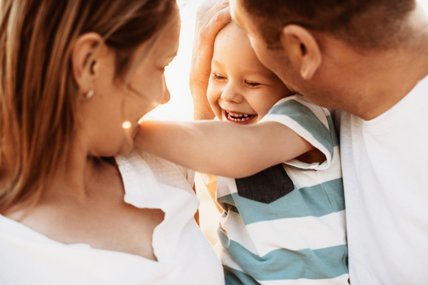 Parents hugging and kissing a laughing child outdoors.