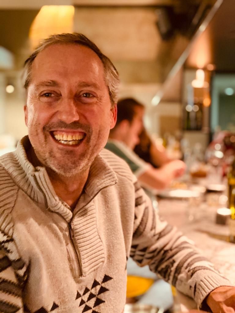 a man in a sweater is smiling while sitting at a table in a restaurant .