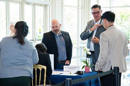 People at a registration table. A man adjusts another's jacket. Other people wait in line.