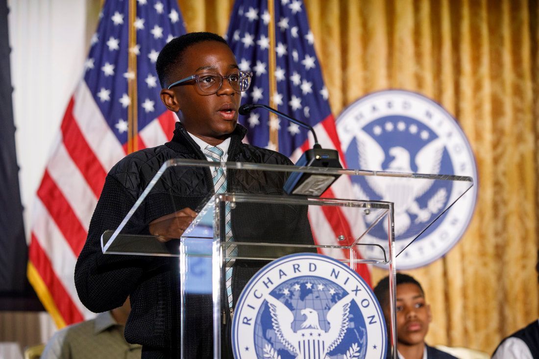 Man speaking at a podium with American flags and a Richard Nixon seal in the background.