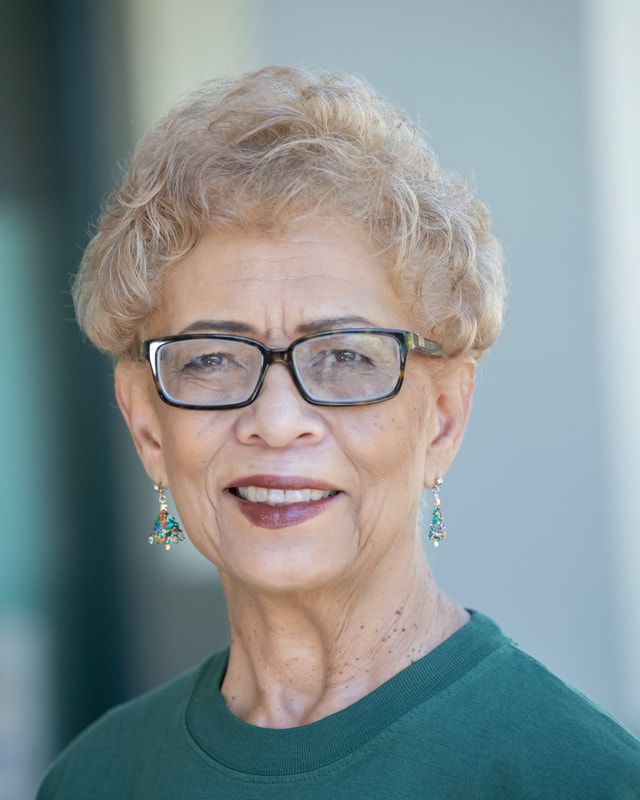 Woman with short, light brown hair wearing glasses and teal earrings, smiling.