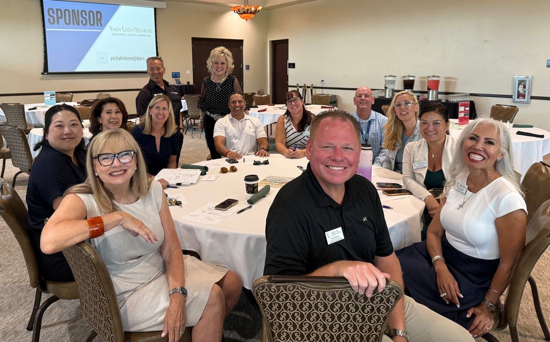 Group of people smiling around a round table in a conference room with a projector screen in the background.