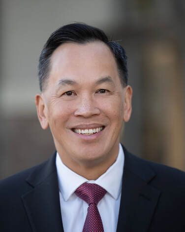 Man in suit and tie smiles, outdoors.