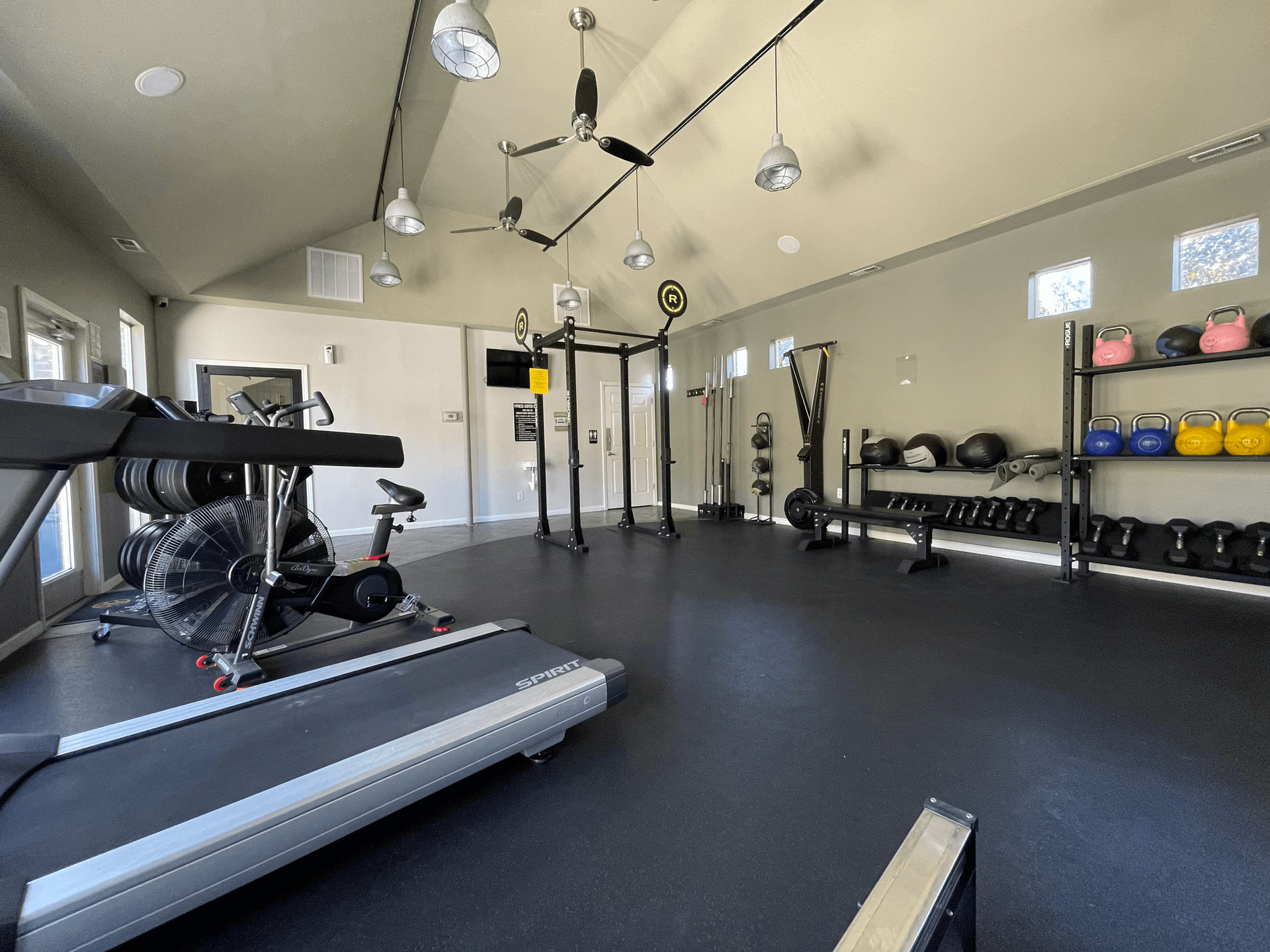 Home gym with treadmill, weight rack, pull-up bar, and weights on black flooring, under angled ceiling.