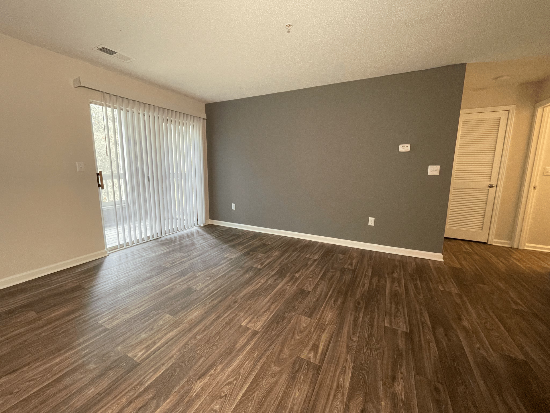 Empty living room with wood flooring, sliding glass door, and a gray accent wall.