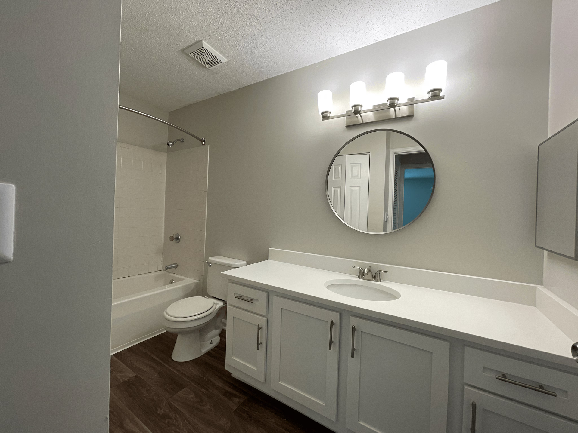 Bathroom with white vanity, round mirror, tub/shower, and gray walls.