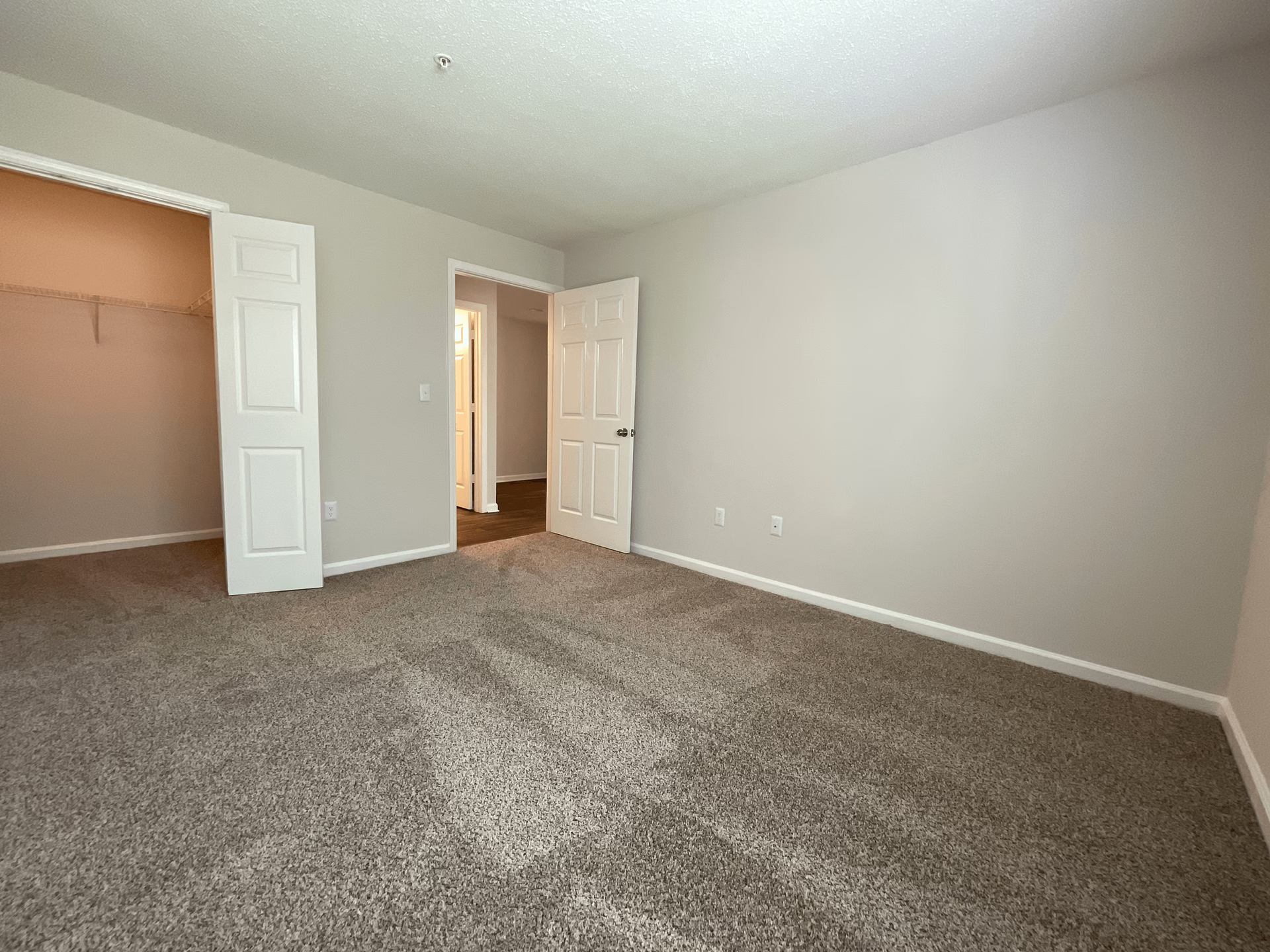 Empty bedroom with tan carpet, neutral walls, closet, and a doorway.