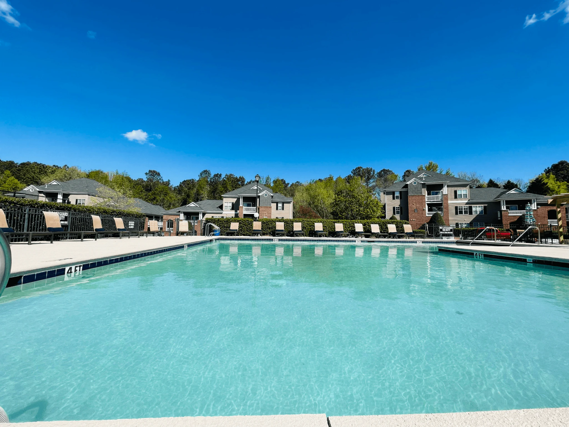 Swimming pool with lounge chairs, apartment buildings, and a bright blue sky.