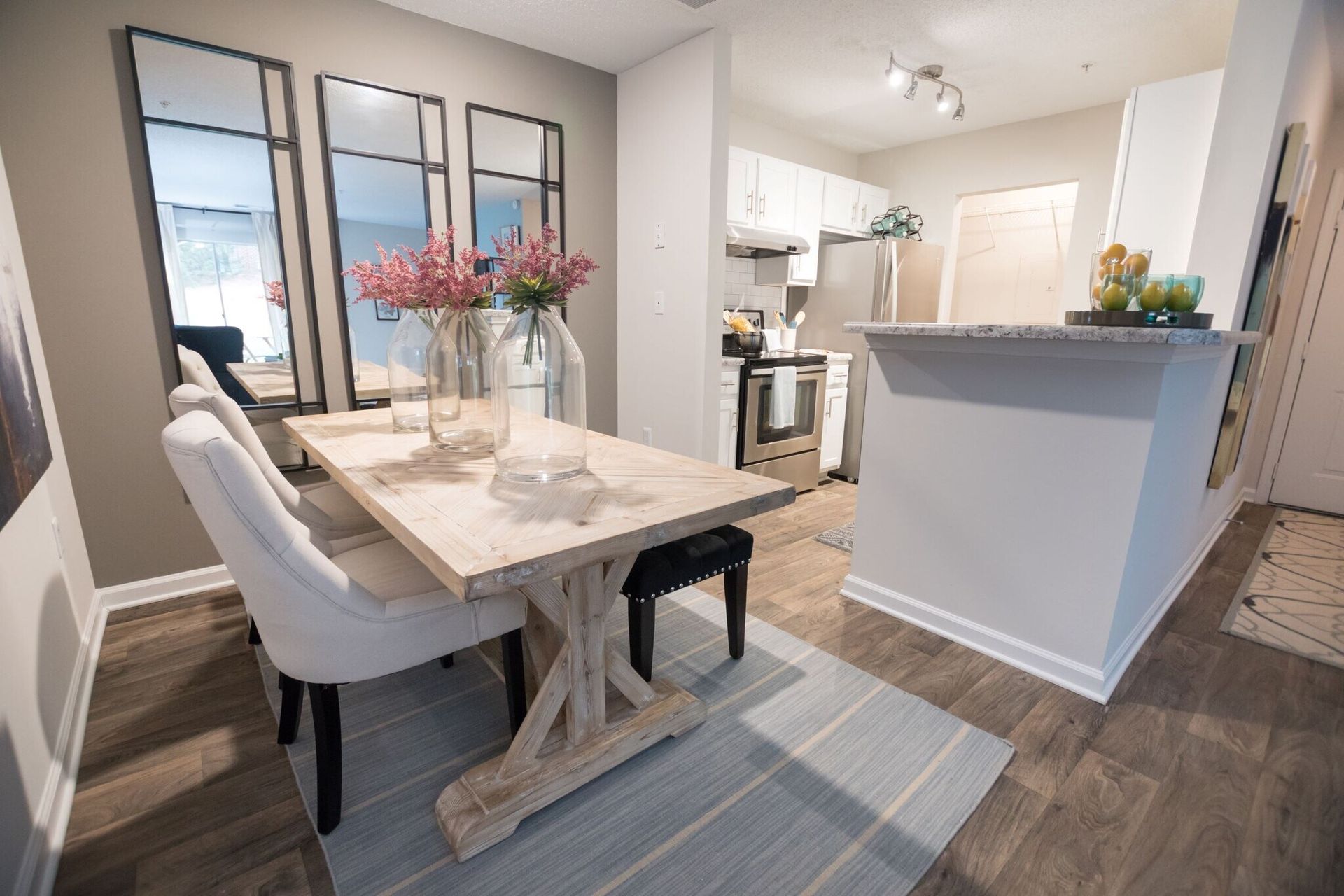 Dining area with table, chairs, mirrors, and open kitchen in the background. Light wood floors, pastel colors.