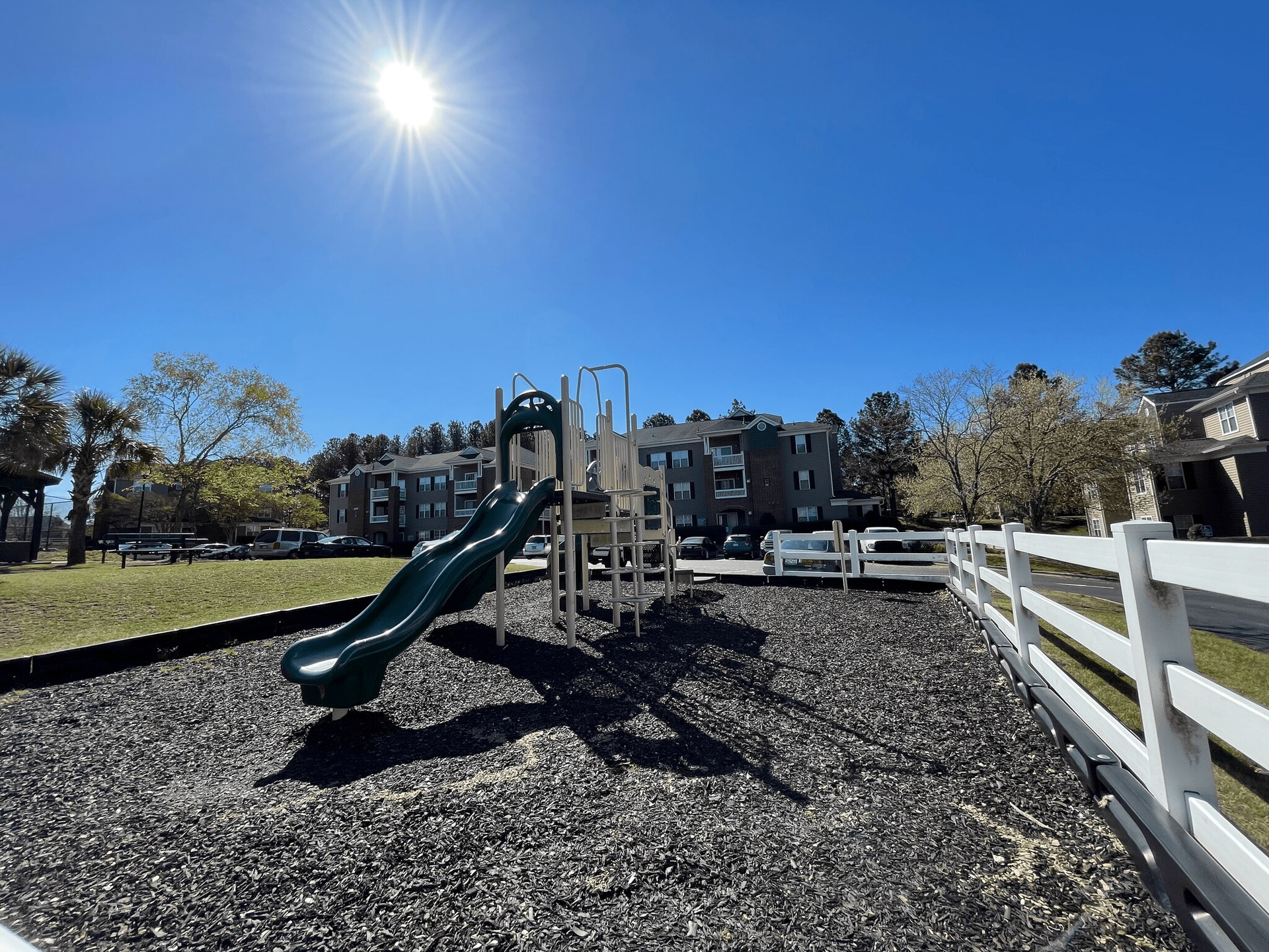 Playground slide with black mulch on a sunny day. Apartment buildings in the background.