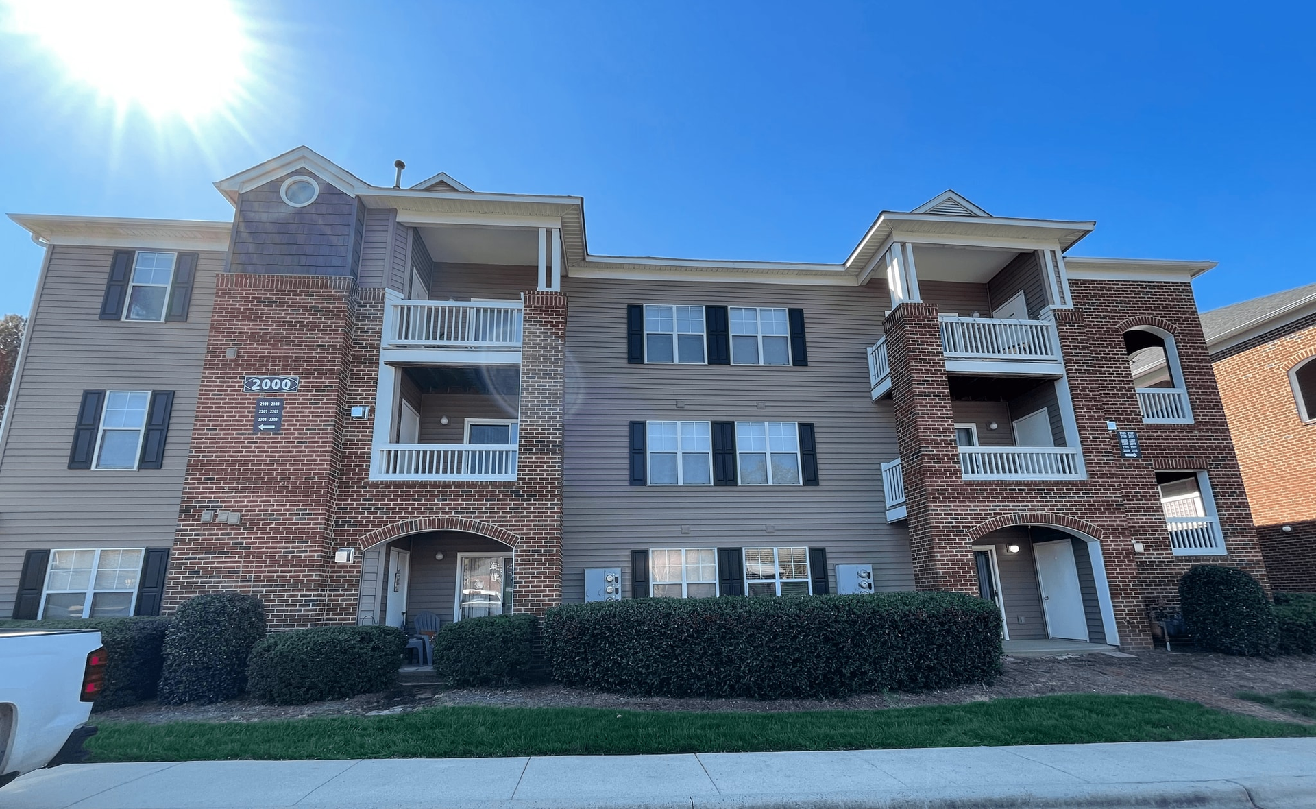 Apartment building with brick accents and balconies under a bright blue sky.
