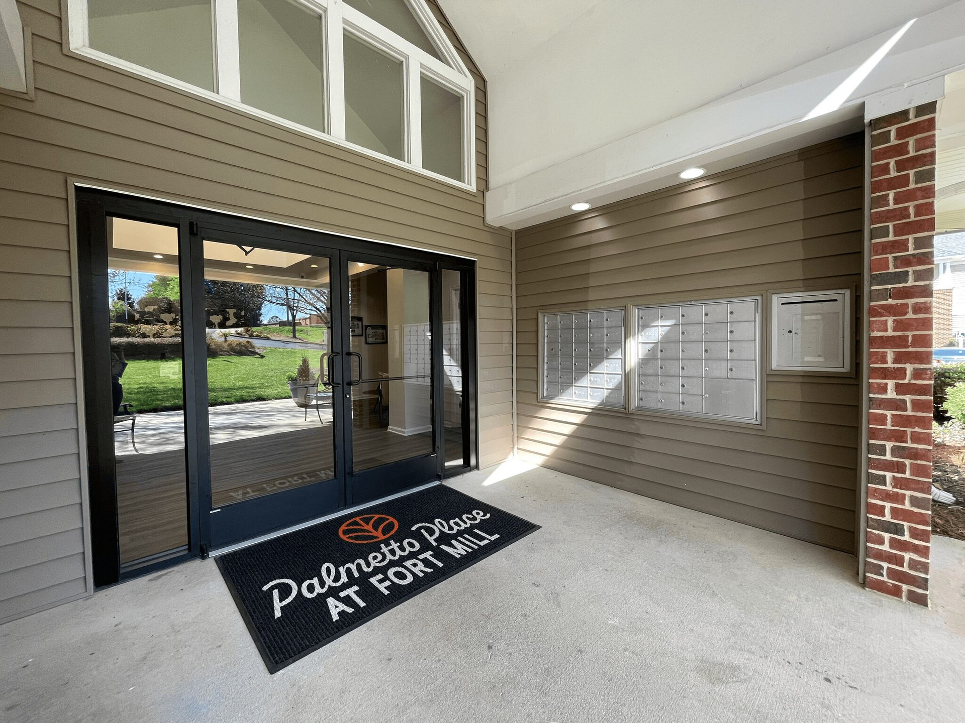 Entrance to Palmetto Place at Fort Mill with glass doors, mailbox and brown siding.
