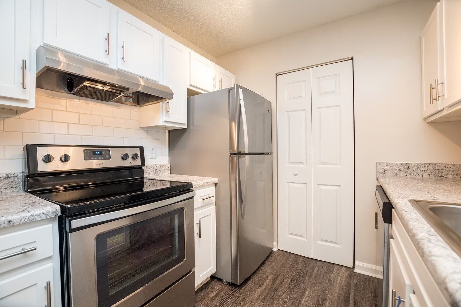 Kitchen with white cabinets, stainless steel appliances, and wood-look flooring.