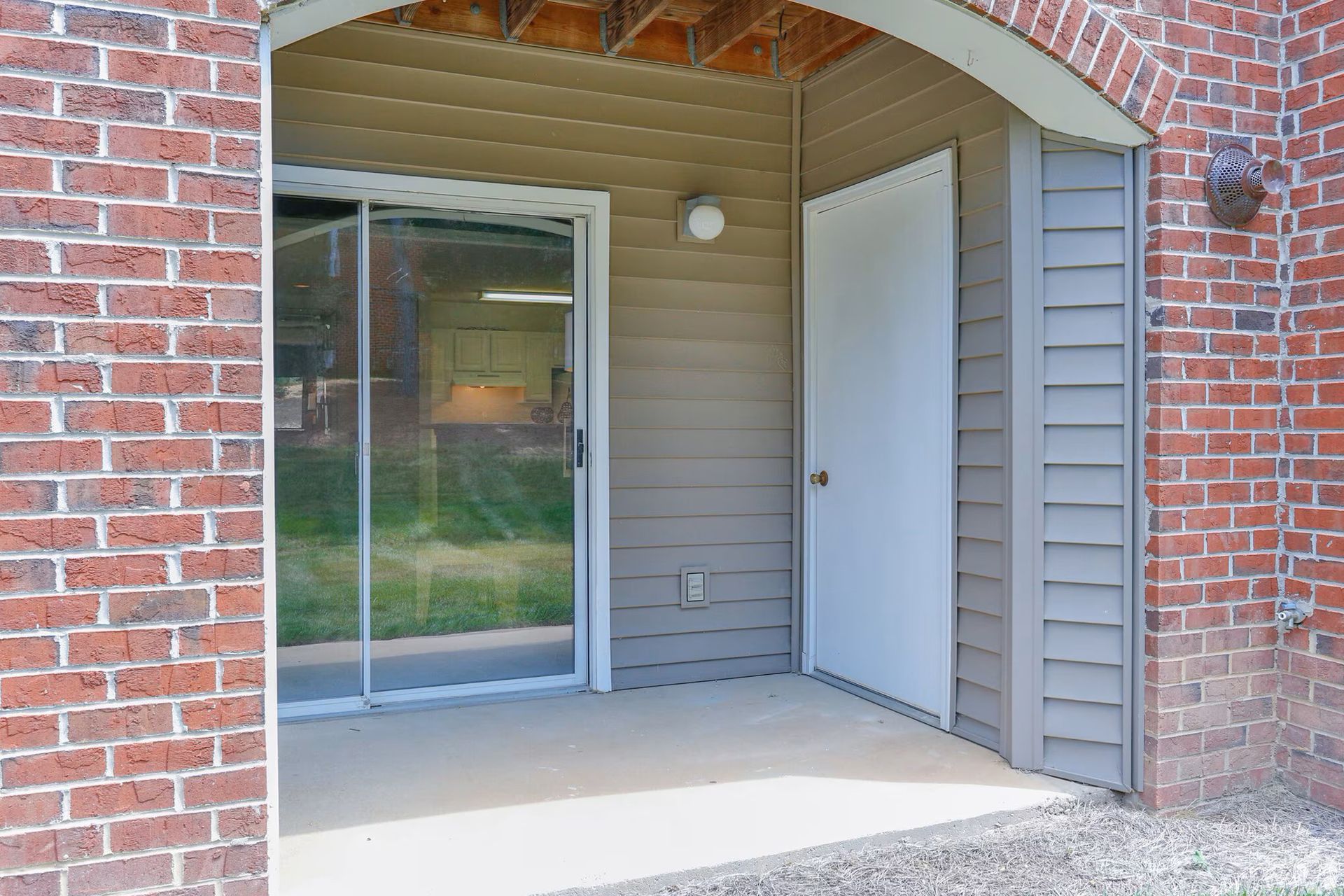 Covered patio with sliding glass door and white door set in a brick and siding exterior.